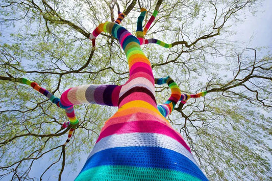 A large tree rises up from the perspective of the viewer. It's trunk and branches are covered in stripes of brightly coloured crochet. Photo by Victoria Bonn-Meuser/ dpa